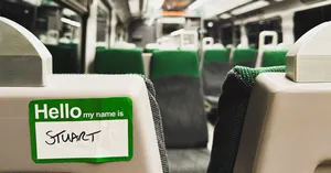 a photo of a sticker that reads Hello my name is Stuart stuck to the back of a seat in an empty train carriage