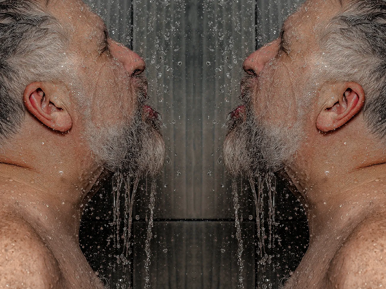 A symetrical image of a man in profile showering, water drips of of his beard