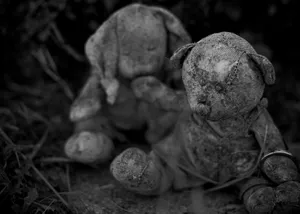 two tattered teddies sitting by the side of a grave