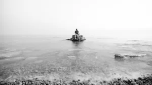 one man sitting on a rock in the ocean