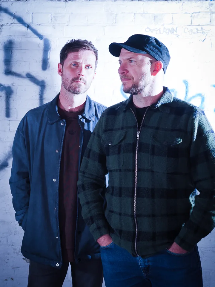 Portrait of Tommy and Darren by a white wall.