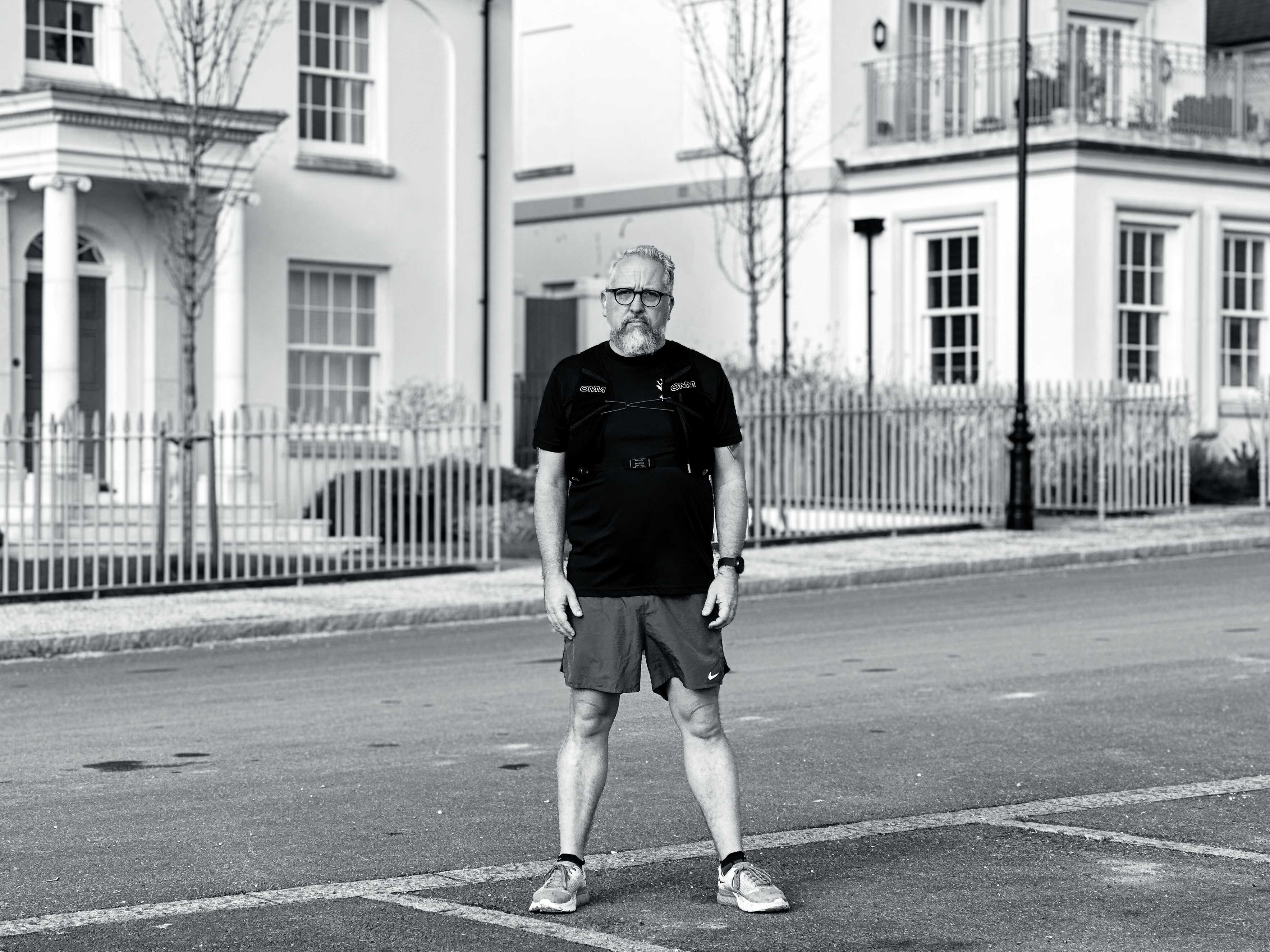 Stuart stands in the road in front of some nice white rendered houses in his running attire looking a bit grumpy