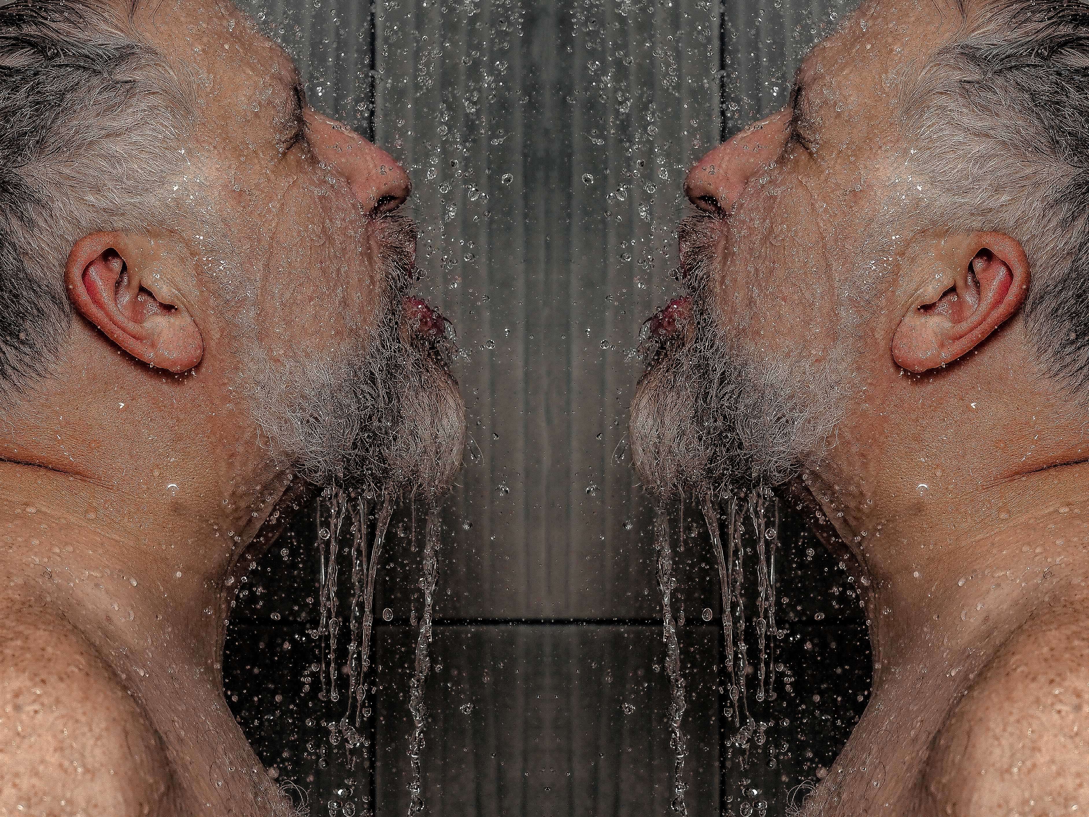 A symetrical image of a man in profile showering, water drips of of his beard